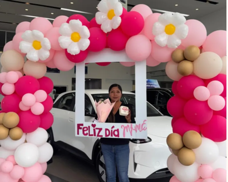 Arco de globos y marco fotográfico junto a un vehículo en el showroom de Geely Metepec